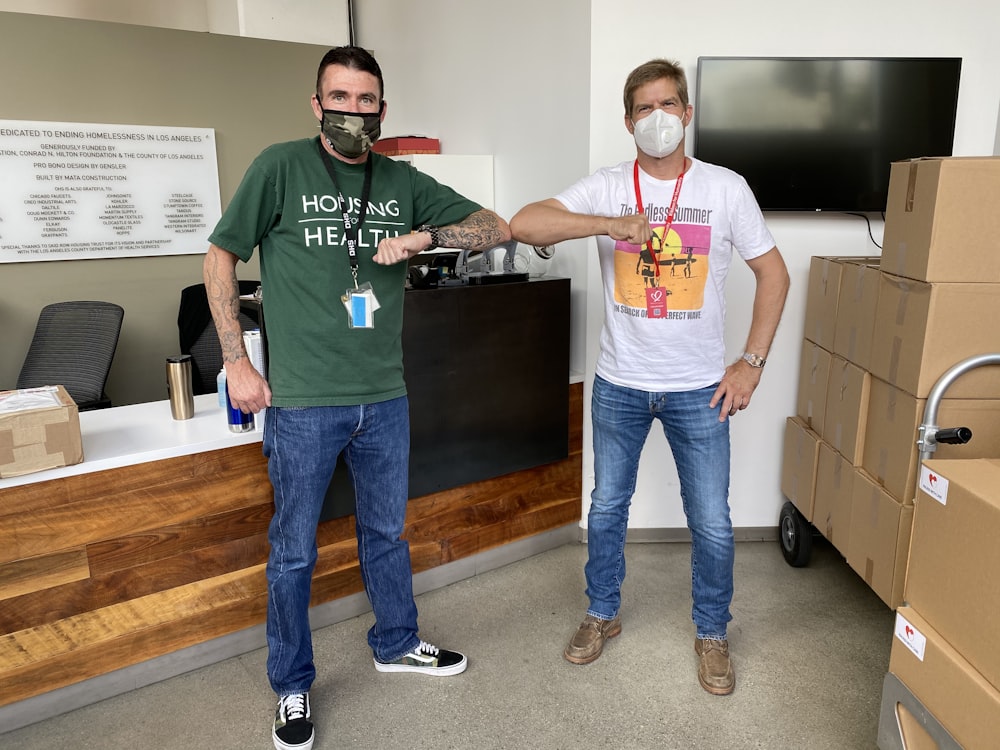 man in green crew neck t-shirt and blue denim jeans standing near black flat screen