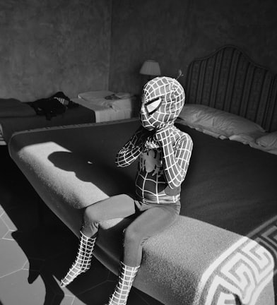 child wearing Spider-Man costume in act of finishing putting on mask while sitting on bed