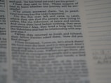 A close-up of a page from a religious text, possibly a Bible, with text involving a conversation about a priest's response and journey. The text appears slightly blurred along the edges.