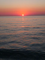 Sunset over the Mediterranean coast with warm orange and pink hues reflecting on the calm sea.