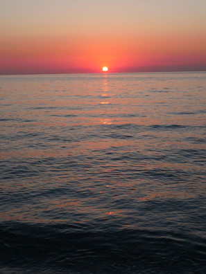 Sunset over the Mediterranean coast with warm orange and pink hues reflecting on the calm sea.