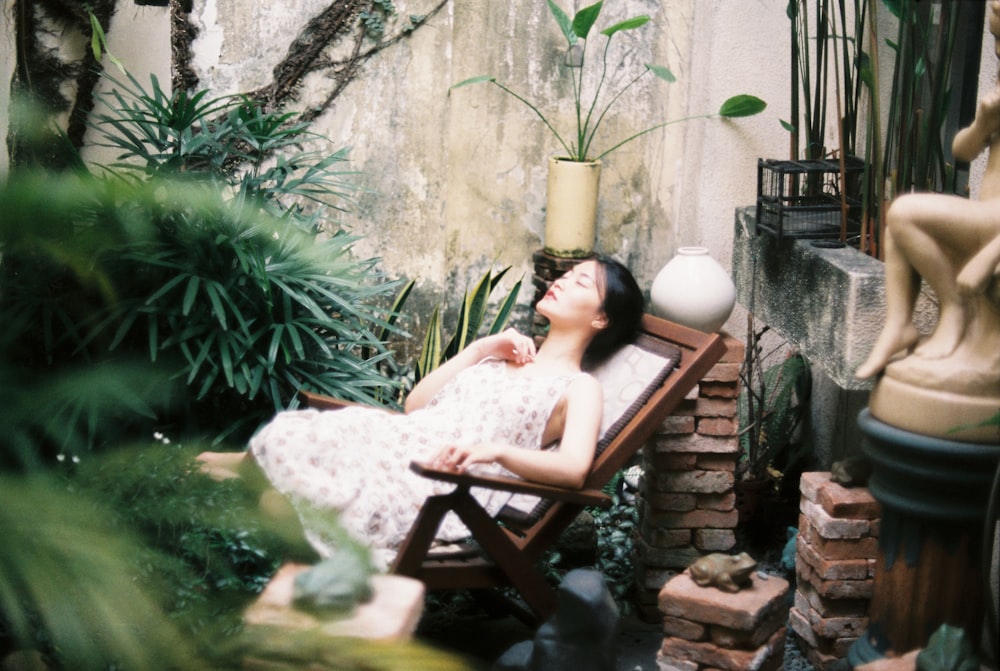 woman in white and black floral dress lying on brown wooden lounge chair