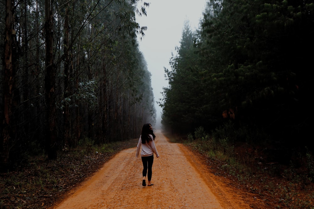 昼間、緑の木々の間の未舗装の道を歩く黒いジャケットの女性