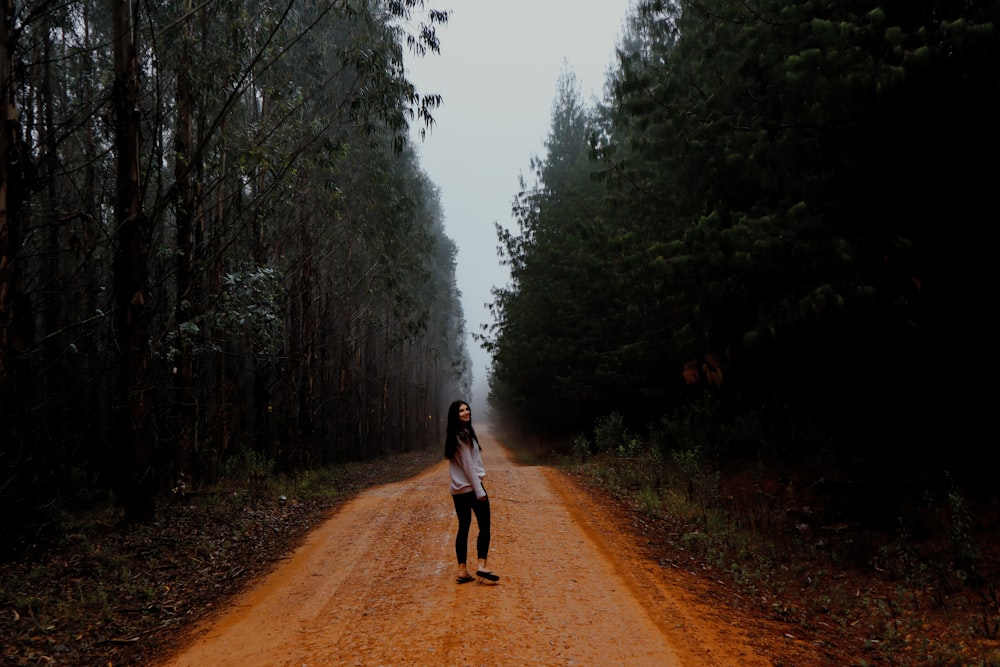 woman in white jacket walking on dirt road between trees during foggy weather