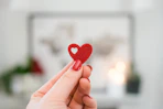Close-up of hands holding a red heart-shaped donation box with a white background.