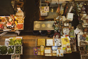 An overhead view of a market stall displaying spices, textiles, sports equipment, and fresh farm products all together.