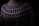 A close-up of a knitted sweater with intricate geometric patterns in black and white. The sweater has a high neckline and showcases various zigzag and dot designs. The lighting is dim, creating a cozy and warm atmosphere.