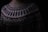 A close-up of a knitted sweater with intricate geometric patterns in black and white. The sweater has a high neckline and showcases various zigzag and dot designs. The lighting is dim, creating a cozy and warm atmosphere.