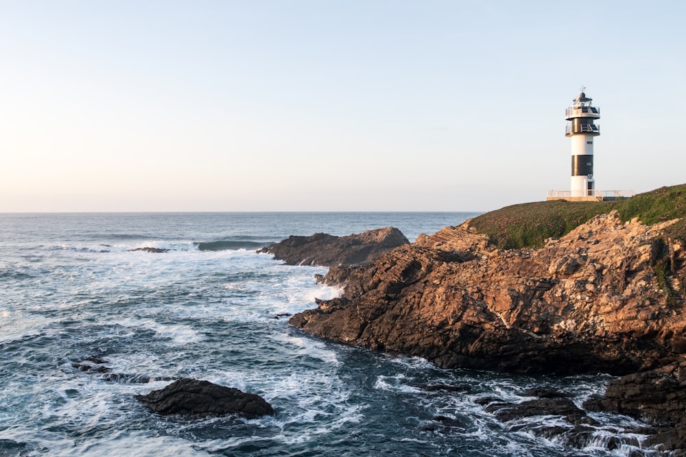 brown and white lighthouse on brown and green hill near body of water during daytime