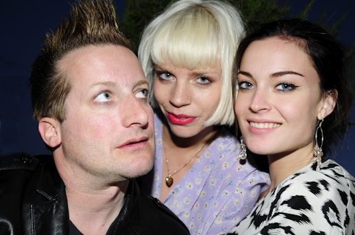 Three individuals are closely grouped together, each displaying distinct hairstyles and expressions. The person on the left has short spiky hair and is glancing upwards. The central figure has a blonde bob haircut, wearing light makeup, and appears to be looking directly at the camera. The person on the right has dark hair pulled back, bright eyes, and is smiling, wearing hoop earrings. They are all in casual attire and seem to be enjoying themselves.