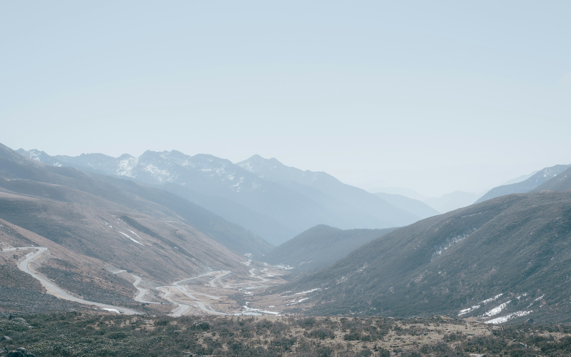 A panoramic view of a winding mountain road disappearing into mist, captured in soft morning light.