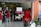 A storefront with glass doors displaying mannequins wearing red dresses. The shop sign reads 'TAILOR MADE' with additional signage about discounts and payment options. A scooter is parked outside along with a shelf of bottled water.