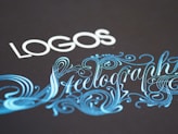 Elegant typography featuring the word 'LOGOS' in white capital letters, paired with an ornate script of 'Steelography' in a flowing, decorative blue font against a dark background.