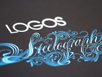 Elegant typography featuring the word 'LOGOS' in white capital letters, paired with an ornate script of 'Steelography' in a flowing, decorative blue font against a dark background.