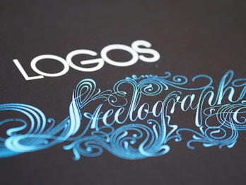 Elegant typography featuring the word 'LOGOS' in white capital letters, paired with an ornate script of 'Steelography' in a flowing, decorative blue font against a dark background.