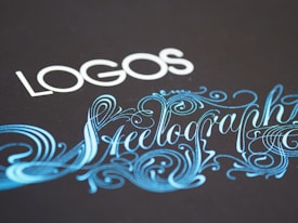 Elegant typography featuring the word 'LOGOS' in white capital letters, paired with an ornate script of 'Steelography' in a flowing, decorative blue font against a dark background.