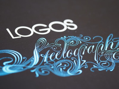 Elegant typography featuring the word 'LOGOS' in white capital letters, paired with an ornate script of 'Steelography' in a flowing, decorative blue font against a dark background.