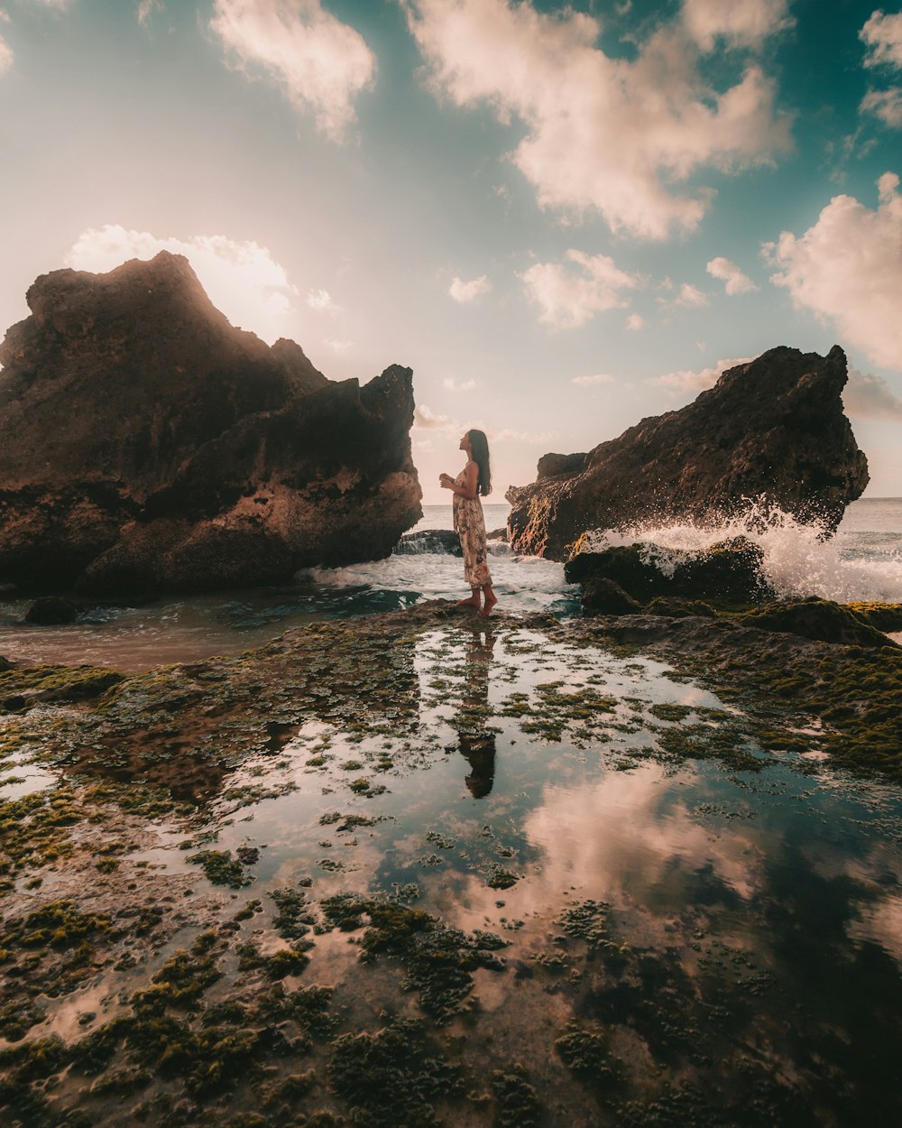 person standing on rock formation in the middle of sea during daytime