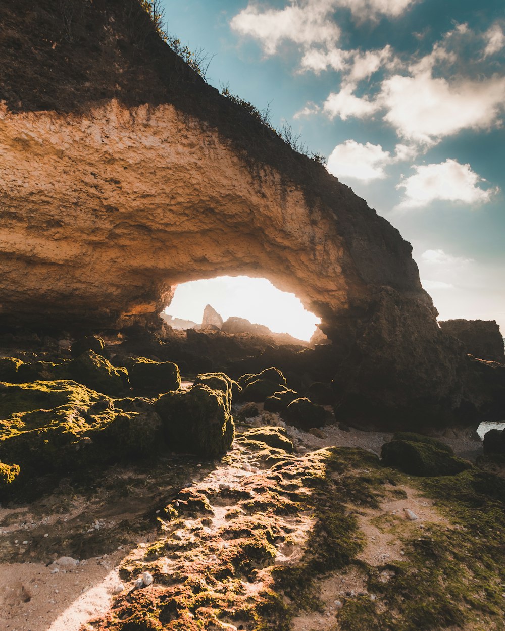the sun is shining through a cave on the beach