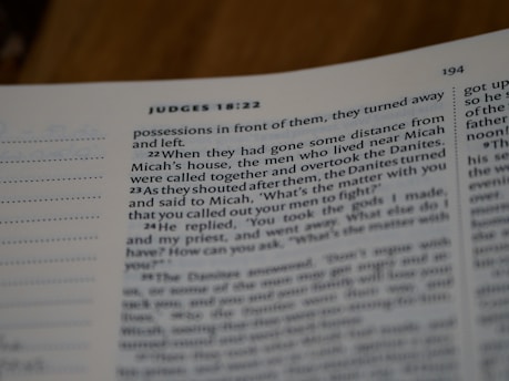 A close-up view of an open book, showing a passage from the Bible, specifically from the book of Judges. The focus is on the text, with sentences and verse numbers clearly visible. The lighting creates a gentle shadow over the page.