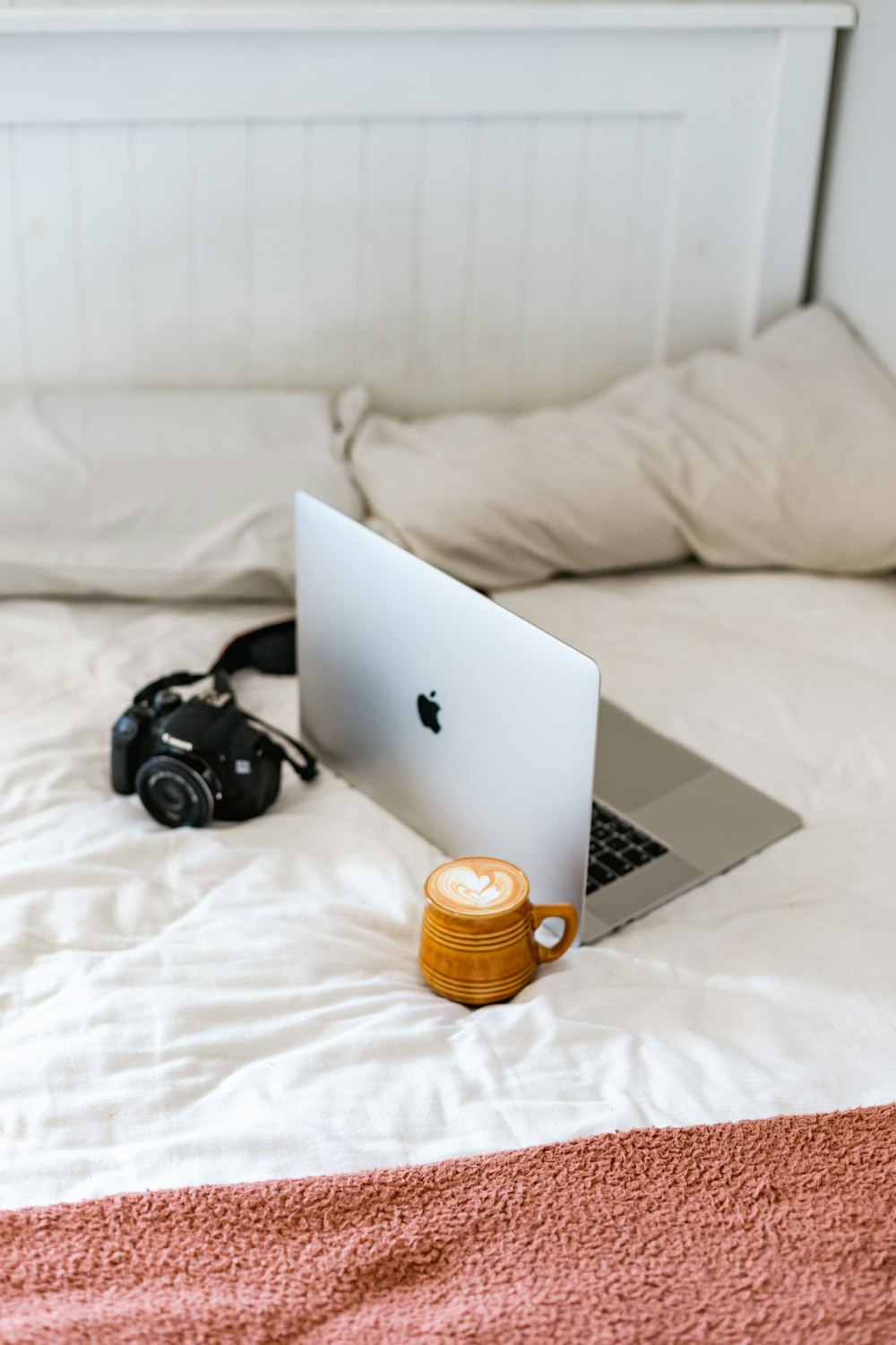 black and silver headphones beside silver macbook on white bed