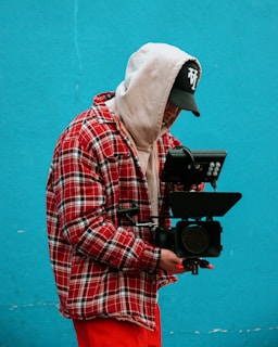 man in red white and black plaid dress shirt holding black dslr camera