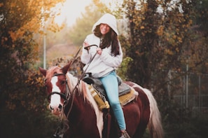 An equestrian wearing a stylish hoodie while grooming a horse.