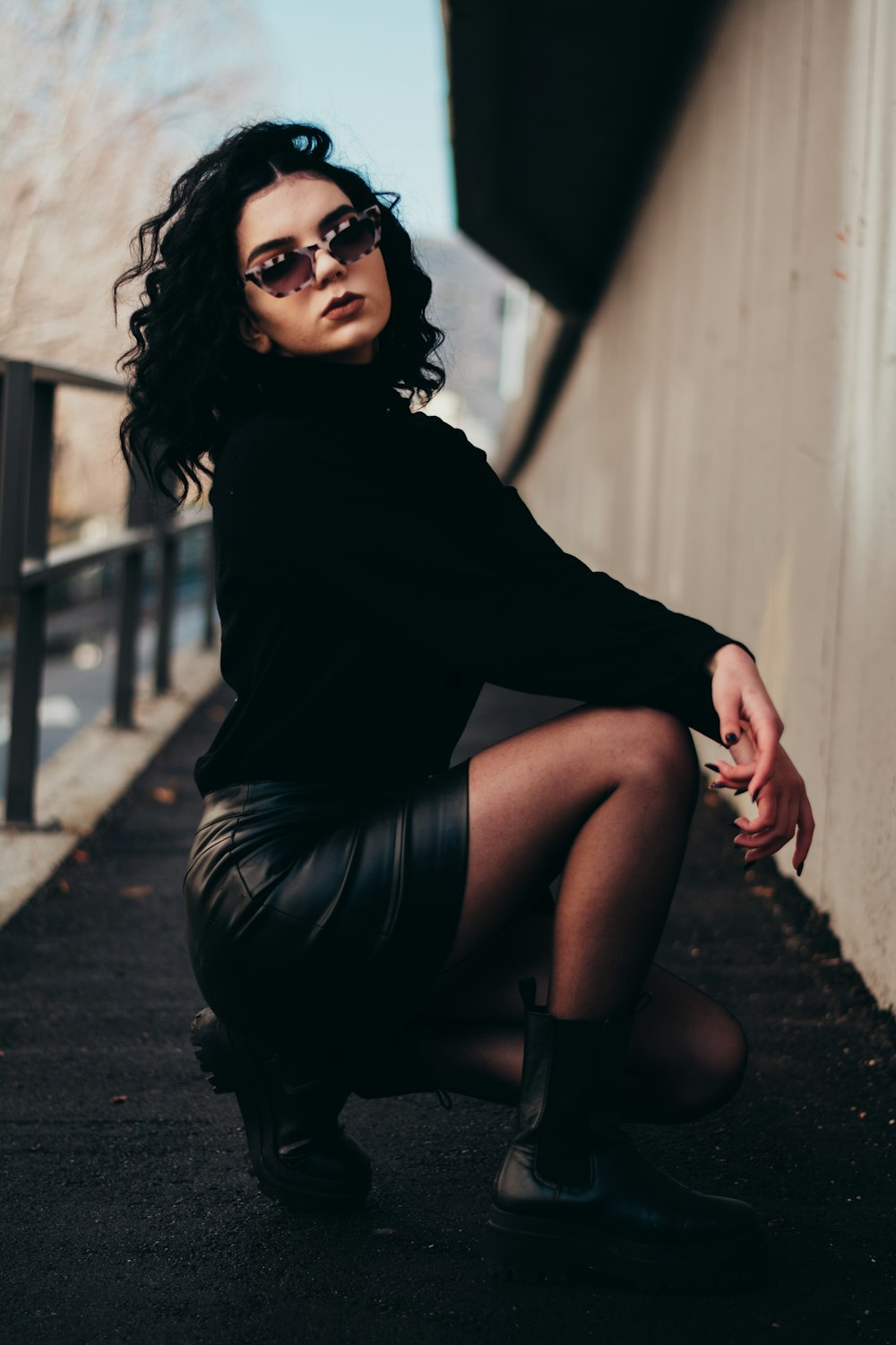 woman in black long sleeve shirt and black skirt sitting on sidewalk during daytime