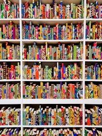 A series of bookshelves filled with books that have vividly patterned and colorful covers. The books are arranged neatly, creating a visually striking display of geometric and abstract designs. Each book seems to have a unique combination of colors and patterns, ranging from stripes and dots to floral and geometric motifs.
