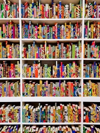 A series of bookshelves filled with books that have vividly patterned and colorful covers. The books are arranged neatly, creating a visually striking display of geometric and abstract designs. Each book seems to have a unique combination of colors and patterns, ranging from stripes and dots to floral and geometric motifs.
