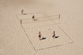 Players diving for the ball on a sandy beach volleyball court.