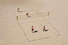 Players diving for the ball on a sandy beach volleyball court.