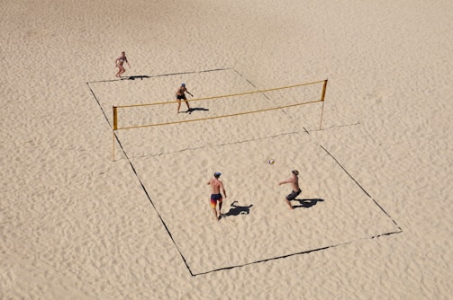 Close-up of players diving for the ball on a sunlit sand court.