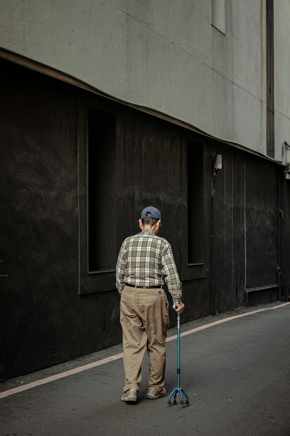 hombre en camisa de vestir a cuadros blanco y negro y pantalones marrones de pie frente a negro