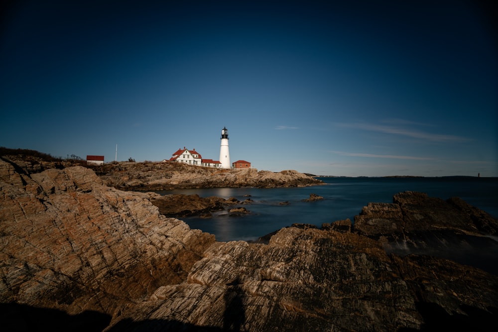 white lighthouse on brown rock formation near body of water during daytime