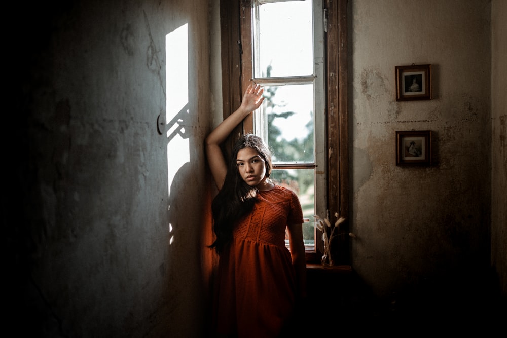 woman in orange dress standing near window