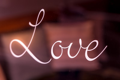 The word 'Love' is written in elegant, cursive white script against a dark, blurred background. The letters are smoothly connected, forming a visually pleasing flow.