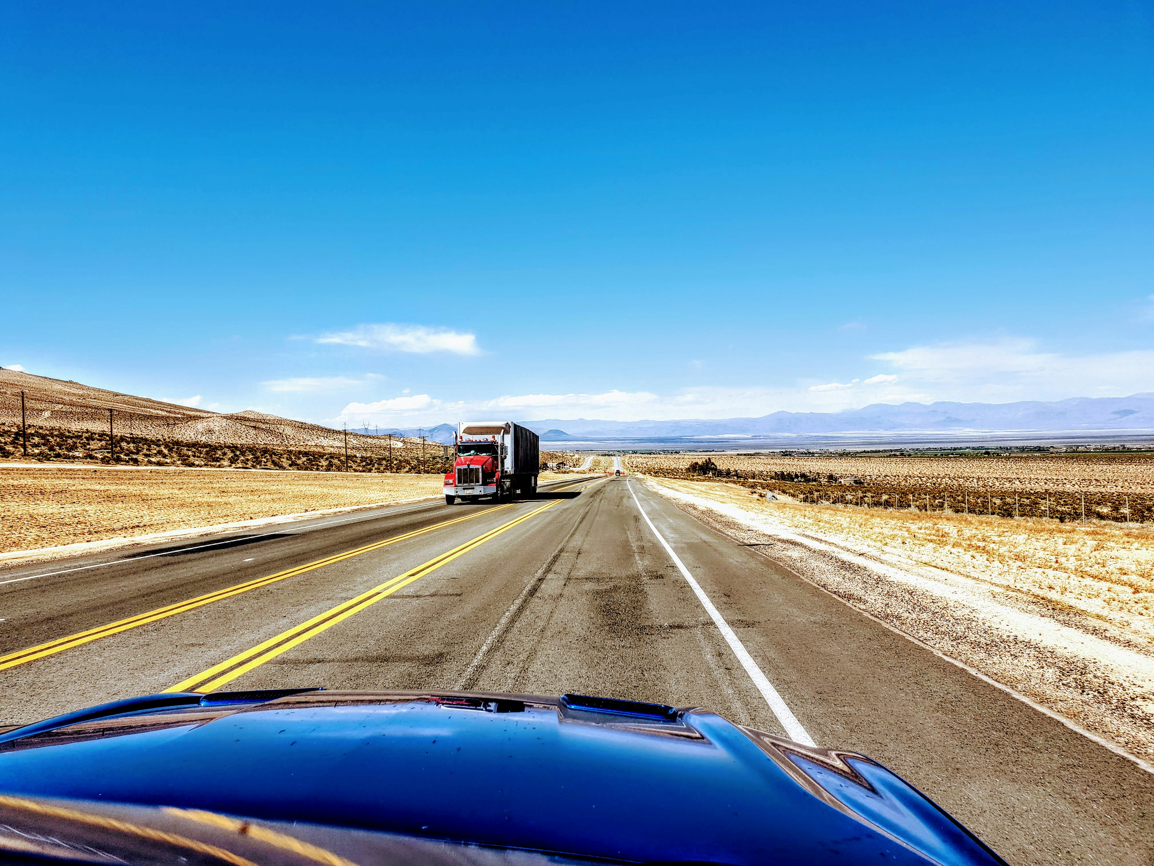 Full semi-truck on open interstate highway, clear blue sky, daytime, wide shot