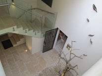 A modern interior featuring a staircase with glass railings and stone tile flooring. A decorative metallic sculpture resembling a tree is prominently displayed near a wall adorned with abstract metallic leaves. Subdued lighting creates a soft ambiance.