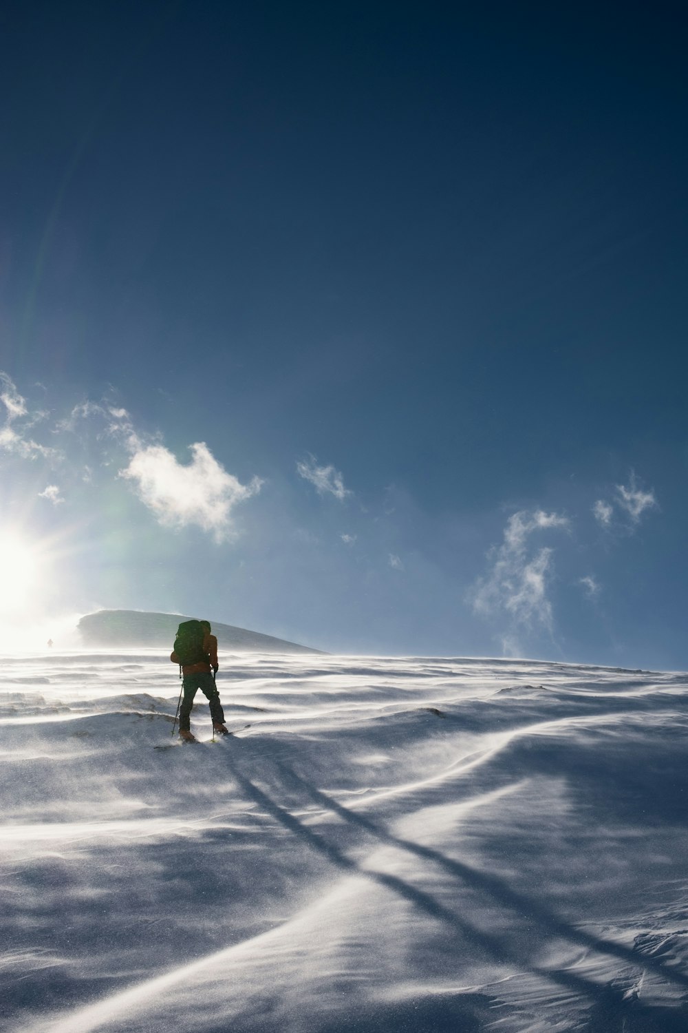 person in green jacket walking on snow covered ground under blue and white sunny cloudy sky