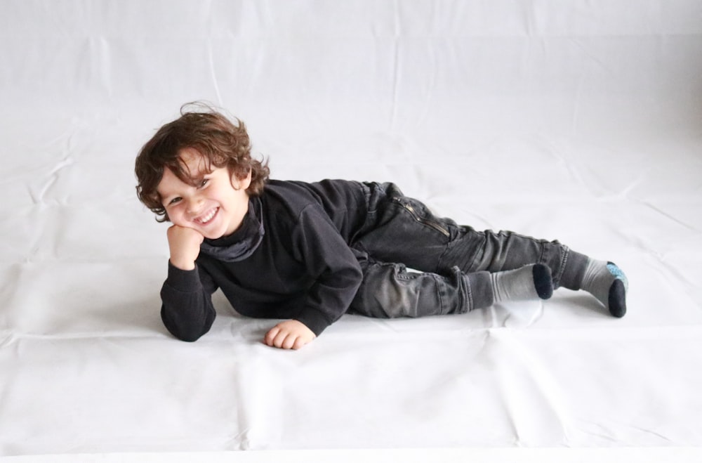 boy in black leather jacket lying on white bed