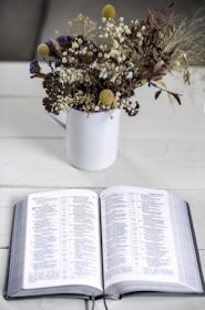 An open Bible beside a cup of herbal tea and a small vase of fresh flowers.