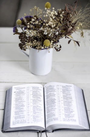An open Bible resting on a wooden table surrounded by fresh flowers.