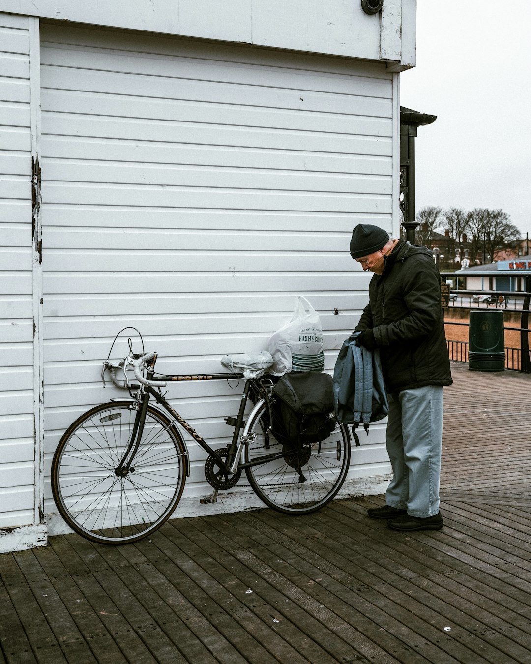 man in green jacket and gray pants standing beside black city bike during daytime