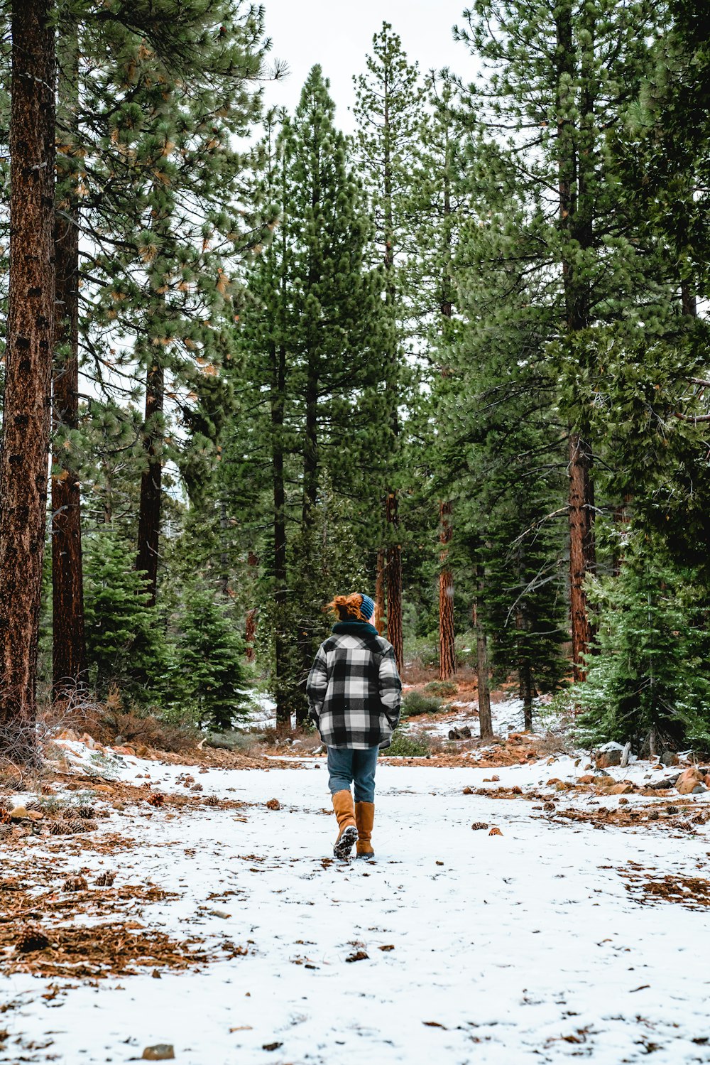 Hombre con chaqueta a cuadros azul y blanco y jeans de mezclilla azules caminando por un camino cubierto de nieve