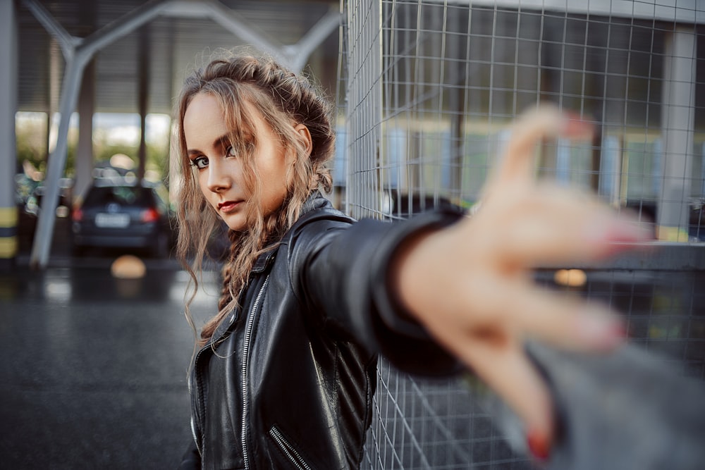 woman in black leather jacket standing beside gray metal fence during daytime