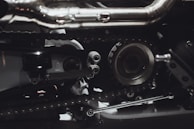 Intricate mechanical components featuring gears, chains, and metal parts, likely part of an engine or machinery. The image highlights metallic textures and detailed craftsmanship.