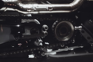 Intricate mechanical components featuring gears, chains, and metal parts, likely part of an engine or machinery. The image highlights metallic textures and detailed craftsmanship.