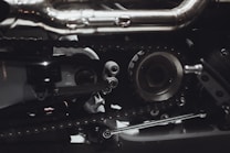 Intricate mechanical components featuring gears, chains, and metal parts, likely part of an engine or machinery. The image highlights metallic textures and detailed craftsmanship.