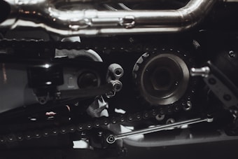 Intricate mechanical components featuring gears, chains, and metal parts, likely part of an engine or machinery. The image highlights metallic textures and detailed craftsmanship.